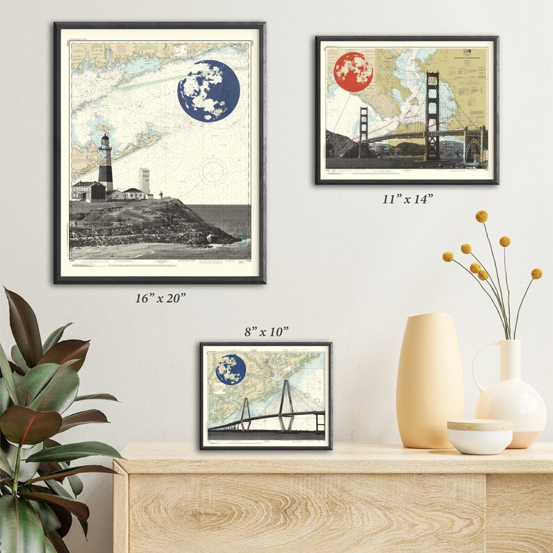 May include: Three framed prints of nautical maps with a red and blue moon superimposed over the Golden Gate Bridge, a lighthouse, and a bridge. The prints are in black frames and are displayed on a wooden shelf.