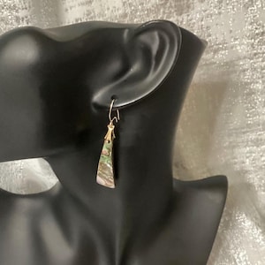 May include: A single gold-colored earring with a rectangular abalone shell pendant. The pendant has iridescent green, pink, and brown hues. The earring is displayed on a black mannequin head.