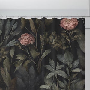 May include: Shower curtain with a dark background and a botanical print. The design features large leaves and flowers in shades of green, gray, and dusty rose. The curtain is hanging from a white shower rod.