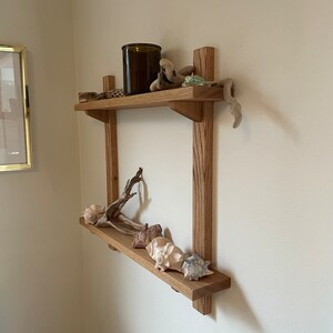 May include: A two-tiered wooden shelf with a dark brown glass jar on the top shelf and seashells and driftwood on both shelves.