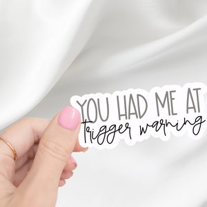 May include: White sticker with black text that reads "You had me at trigger warning".