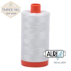 May include: A spool of Aurifil Mint Ice 2800 thread. The thread is a light, cool gray color, wound around a white spool with a red base and top. The image includes the Timber Hill Sew Shop logo and the Aurifil logo.