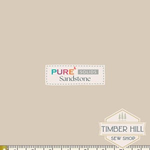 May include: Sandstone fabric with the text "PURE SOLIDS Sandstone" in a stitched label. A measuring tape shows inches. The Timber Hill Sew Shop logo is also visible. The fabric is a solid, neutral beige color.