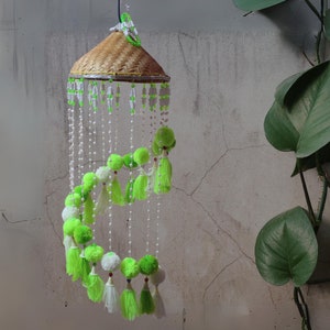 May include: A green and white hanging mobile with pom-poms and beads. The mobile is made of natural materials and has a woven top.