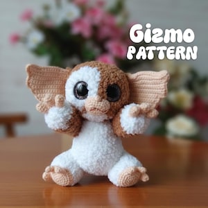 May include: A handmade crochet figure of Gizmo from the movie Gremlins. The plush toy is white and brown with large black eyes and tan ears and feet. The text "Gizmo PATTERN" is in white script.