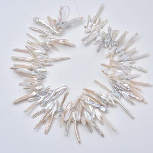 May include: A necklace composed of irregularly shaped, white and iridescent freshwater pearls. The pearls are strung together, forming a circular shape. The pearls have a natural, organic appearance, with variations in color and texture.