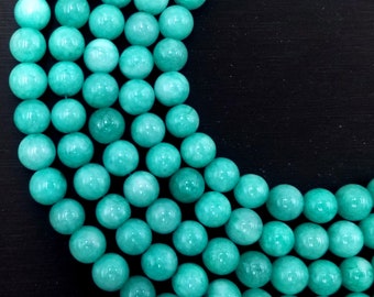 Peut inclure: Un brin de perles de jade vert turquoise. Les perles sont rondes et lisses, et elles sont disposées en cercle.