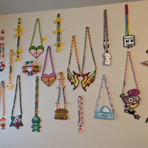 May include: A wall decorated with colorful beaded necklaces featuring various cartoon characters, including a burger, a bird, a ghost, and a marshmallow. The necklaces are made of plastic beads and are strung together in different patterns.