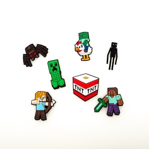 May include: A collection of colorful Minecraft character charms, including a green Creeper, a black spider, and a TNT block. Other characters include a Steve with a sword, an archer, a character riding a chicken, and an Enderman.