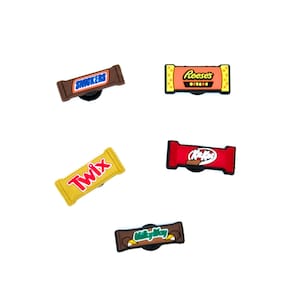 Op de afbeelding: Collectie snoepreep bedels, waaronder Snickers, Reese's, Twix, Kit Kat en Milky Way. Elke bedel toont het logo en de verpakking van het merk, met een zwarte basis voor bevestiging.