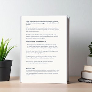 May include: A book titled "Fear to Flush" with text about toilet training for children and parents. The book's cover is white with black text. The book is next to a potted plant and other books.