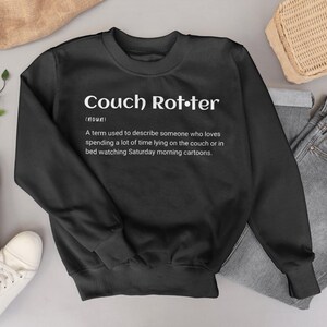 May include: Black sweatshirt with the text "Couch Rotter" in white, with a definition below. The definition describes someone who loves spending time on the couch or in bed watching Saturday morning cartoons.