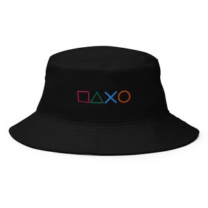 May include: Black bucket hat with embroidered colorful PlayStation controller symbols. The symbols include a pink square, green triangle, blue X, and orange circle. The hat has a wide brim and a classic bucket hat shape.
