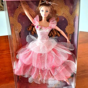 May include: A Barbie doll from the Collector Edition Classic Ballet Series in its original packaging. The doll has brown hair and wears a pink satin bodice with floral accents and a multi-layered pink and silver glittery tulle skirt.