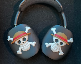 Può includere: Cuffie wireless nere con un design a forma di teschio e ossa incrociate con un cappello di paglia e una fascia rossa. Il teschio è bianco con un contorno nero.