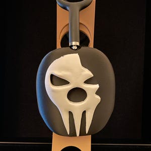 Pu&ograve; includere: Un supporto per cuffie a forma di teschio nero e bianco con un design a teschio bianco. Il supporto &egrave; realizzato in plastica stampata in 3D e ha un gancio nero nella parte superiore.