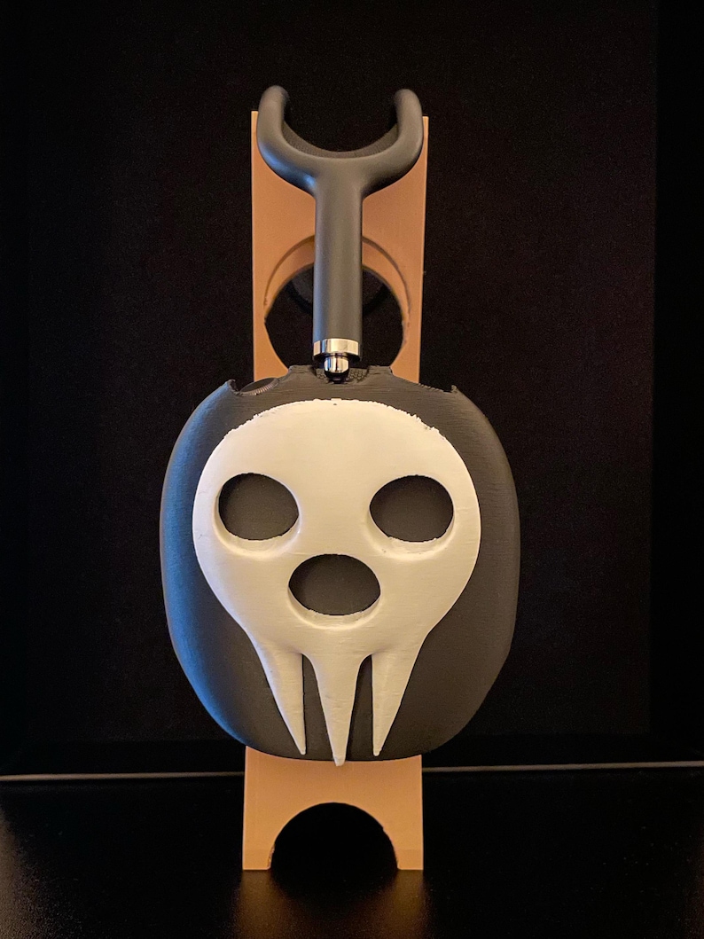 Pu&ograve; includere: Un supporto per cuffie a forma di teschio nero e bianco con un design di teschio bianco. Il supporto &egrave; in plastica e ha una base nera.