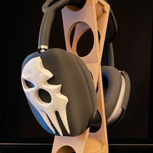 Pu&ograve; includere: Un supporto per cuffie in legno con un design a teschio bianco e nero su una delle cuffie.
