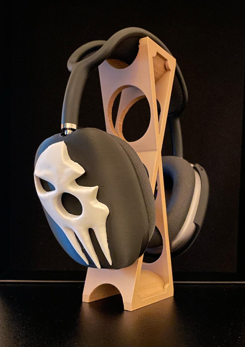 Pu&ograve; includere: Un supporto per cuffie in legno con un design a teschio bianco e nero su una delle cuffie.