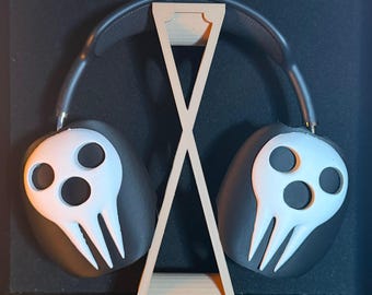 Può includere: Cuffie nere con disegni di teschi bianchi sui padiglioni auricolari, appoggiate su un supporto per cuffie in legno marrone chiaro. Il supporto ha un design a forma di X. Lo sfondo è nero.