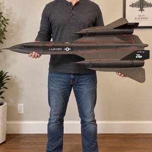 May include: A large black model of an SR-71 Blackbird aircraft featuring red accent lines, the text U.S. AIR FORCE, a star insignia, and the number 17974 on the tail fin. The model has a sleek, elongated design with two prominent engine nacelles.