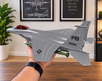May include: A silver model fighter jet with a red cockpit canopy, green missiles mounted under the wings, and the black markings PB 1994 on the vertical stabilizer. The aircraft features a star and bar insignia on the wing and a sleek design.