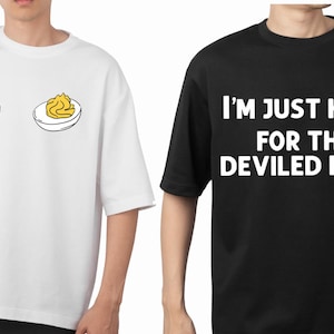 May include: Two t-shirts. One white with a deviled egg design, the other black with the text "I'M JUST HERE FOR THE DEVILED EGGS" in white. Both are short-sleeved and appear to be made of cotton.