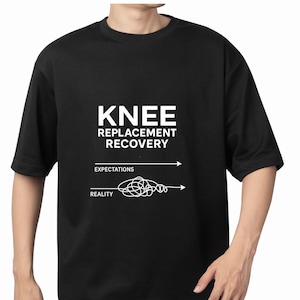 May include: Black t-shirt with the text "KNEE REPLACEMENT RECOVERY" in white. Below the text are the words "EXPECTATIONS" and "REALITY" with corresponding arrows, one straight and one tangled.