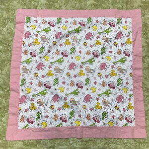 May include: A pink and white baby blanket with a pattern of giraffes, elephants, ducks, and stars. The blanket has a pink border.