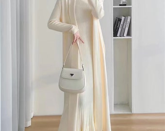 May include: A white knitted cardigan and matching dress with a long, flowing silhouette. The outfit is accessorized with a white handbag and white fur-lined loafers.
