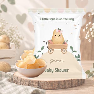 May include: A white snack bag featuring a cartoon potato in a wooden wagon with the text A little spud is on the way, Jessica's Baby Shower. The bag is decorated with small pink flowers and green leaves, with a scalloped pastel border at the top.