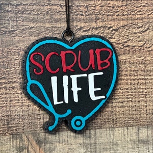 May include: Black heart-shaped ornament with a blue outline. The ornament has a stethoscope design and the words "Scrub Life" written in red and white.