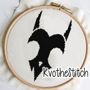 May include: Black and white cross-stitch embroidery of a stylized bat design in a wooden embroidery hoop. The hoop is on a white fabric background. The text "Kvothestitch" is visible in the lower right corner of the image.