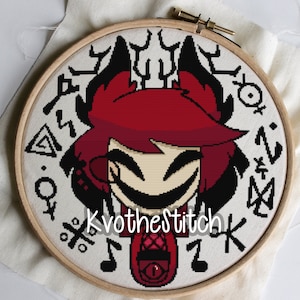 May include: Cross-stitch embroidery hoop with a red-haired character with horns and a mischievous smile. The character is surrounded by black and white symbols and the text "Kvo the Stitch".