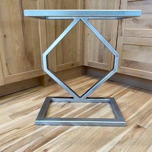 May include: A silver metal table base with a diamond-shaped design. The base has a square top and a rectangular bottom.