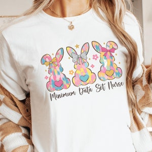 Può includere: Maglietta bianca con una grafica di tre coniglietti colorati e il testo "Minimum Data Set Nurse".