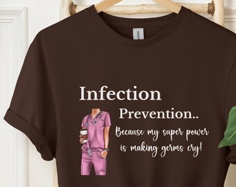 May include: A brown t-shirt with a white graphic of a female nurse holding a cup of coffee. The text on the shirt reads "Infection Prevention.. Because my super power is making germs cry!"
