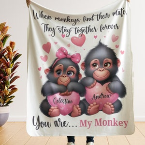 May include: A white fleece blanket with a pink heart design and two cartoon monkeys holding hearts with the names "Celestine" and "Andrew" on them. The text "When monkeys find their mate, They stay together forever" and "You are... My Monkey" is printed on the blanket.