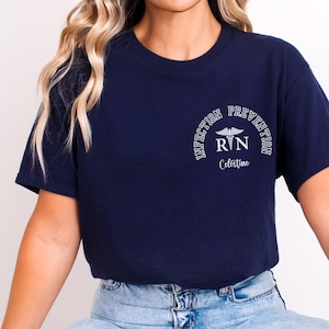 May include: A navy blue t-shirt with a white graphic that says "Infection Prevention RN Celestine" in an arc with a caduceus symbol.