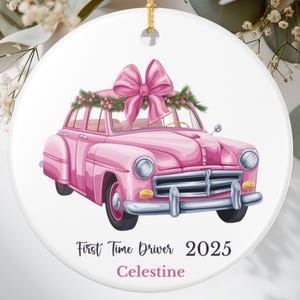 Può includere: Ornamento natalizio in ceramica bianca con un'auto rosa vintage e un grande fiocco rosa. L'ornamento presenta il testo "First Time Driver 2025 Celestine" in nero. Un filo d'oro è attaccato per appenderlo.