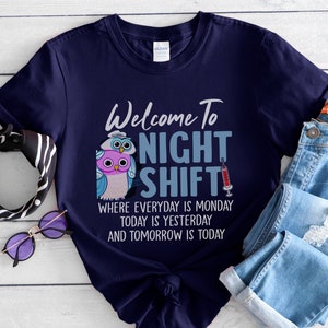 May include: A navy blue t-shirt with a graphic of two owls and a syringe. The text on the shirt reads "Welcome to Night Shift" and "Where everyday is Monday, today is yesterday and tomorrow is today."