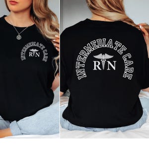 Może przedstawiać: Czarny t-shirt z białym tekstem i symbolem medycznym. Tekst brzmi "INTERMEDIATE CARE" w łuku, z "RN" pod symbolem. Koszulka ma okrągły dekolt.