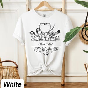 Może przedstawiać: Biała koszulka z czarno-białym nadrukiem przedstawiającym stetoskop, strzykawkę i kwiaty. Na koszulce znajduje się napis "MPS Nurse".