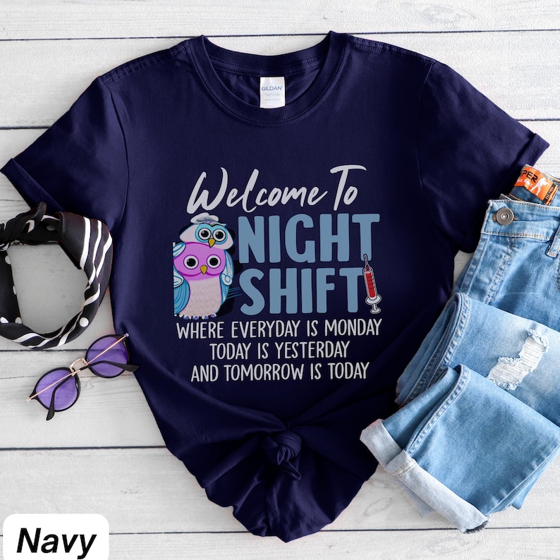 May include: A navy blue t-shirt with a graphic of two owls and a syringe. The text on the shirt reads "Welcome to Night Shift" and "Where everyday is Monday, today is yesterday and tomorrow is today."