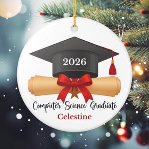 Puede incluir: Adorno de graduación de cerámica blanca con birrete negro, diploma enrollado y lazo rojo. El texto dice "2026", "Computer Science Graduate" y "Celestine". Se adjunta un cordón dorado para colgarlo.