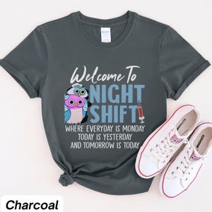 May include: A charcoal gray t-shirt with a graphic of two owls and the text "Welcome to Night Shift" with the tagline "Where everyday is Monday, today is yesterday and tomorrow is today".