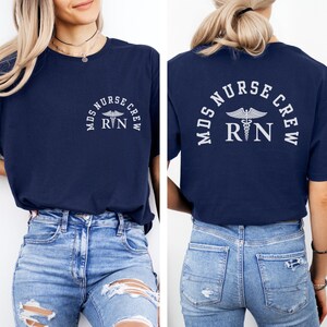 Può includere: T-shirt blu navy con la scritta bianca "MDS NURSE CREW RN", con un simbolo di caduceo. Il disegno è stampato sul davanti e sul retro della maglietta. La maglietta è a girocollo.