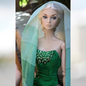 May include: A doll with blonde hair wearing a green dress with a sparkly bodice and a light green sheer scarf.