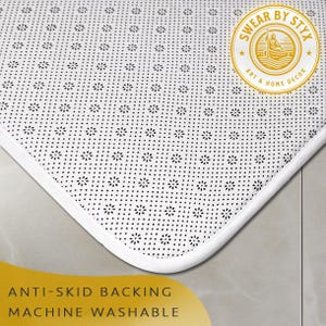 May include: White bath mat with a black non-slip backing. The mat has a white border and the text "Swear by Styx Art & Home Decor" is printed on the mat.