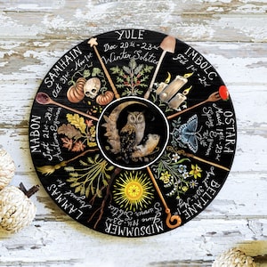 Pode incluir: Uma roda circular preta com oito raios, cada um representando uma &eacute;poca diferente do ano na Roda do Ano. Os raios s&atilde;o etiquetados com os nomes dos oito sabbats: Yule, Imbolc, Ostara, Beltane, Midsummer, Lammas, Mabon e Samhain. Cada raio tamb&eacute;m inclui um intervalo de datas e um s&iacute;mbolo que representa a esta&ccedil;&atilde;o.